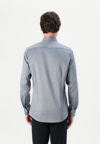 Cămașă de culoare albastră deschisă, cu mânecă lungă, textură netedă, mansete cu butoni și un design structurat pe spate; minimalistă și cu un croi ajustat.