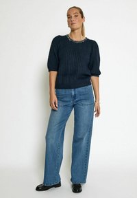 Dark blue knitted sweater with short puff sleeves and a beaded neckline, paired with light blue wide-leg jeans and black shoes.