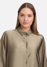 Camicia in satin verde oliva con colletto, chiusura frontale a bottoni e morbida caduta. Maniche lunghe con vestibilità rilassata.