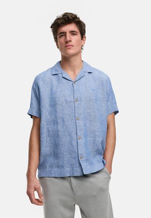 Camisa de manga corta azul claro hecha de lino, con cuello con muesca, botonera delantera y botones de madera natural. Textura suave.