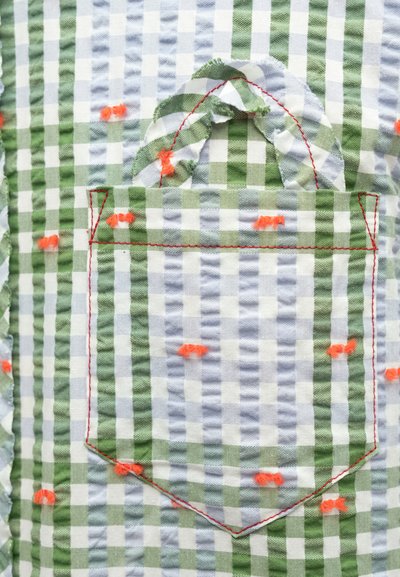 Πράσινο και μπλε υφασμάτινο καρό με ραμμένη πορτοκαλί τσέπη, με φθαρμένες άκρες και κόκκινα ράμματα. Υφή με διακοσμητικά στοιχεία.