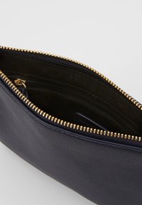 Pochette zippée en cuir bleu marine avec une fermeture éclair dorée. L'intérieur présente une doublure textile sombre et une petite poche zippée pour l'organisation.