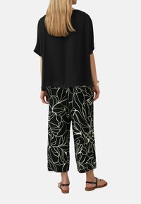 Zwarte T-shirt met korte mouwen en een losse pasvorm, gecombineerd met ruime zwarte broeken met een witte bloemenpatroon en bruine sandalen met banden.
