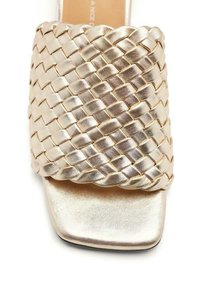 Sandale à glissière tissée en or avec une large sangle texturée et un bout carré. Fini métallique lisse sur la semelle intérieure et la semelle extérieure.