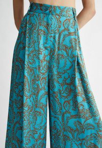 Pantalons larges turquoise ornés d'un imprimé paisley marron, fabriqués dans un tissu lisse et léger avec une taille haute.