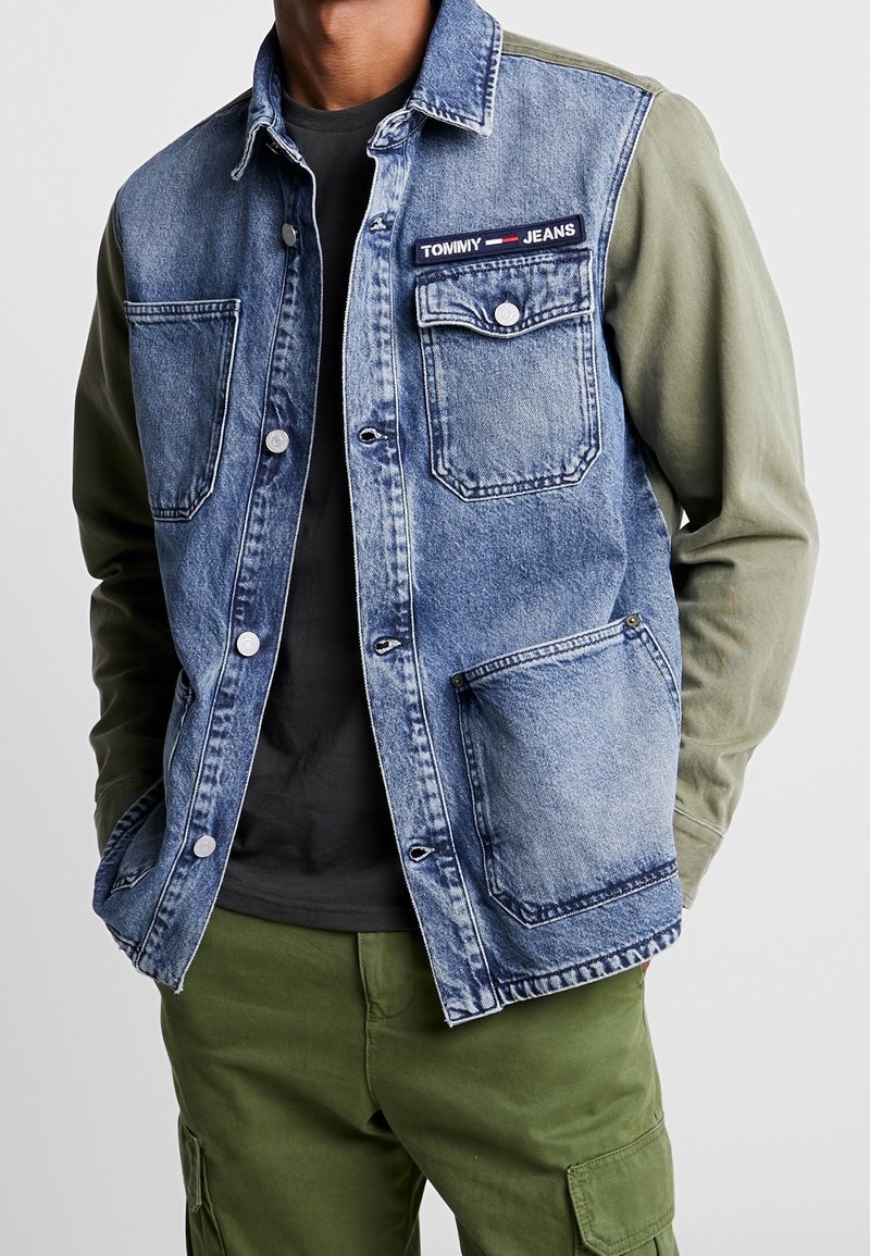 Farkkutakki, jossa on oliivinvihreät hihat, napit ja taskut; rinnassa on "TOMMY JEANS" -patch. Päällä musta paita.