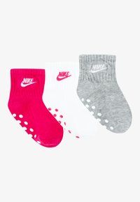 Tre par Nike-strumpor i rosa, vitt och grått. Varje par har ribbad textur och prickiga gripser på sulan, med Nike-logotypen.