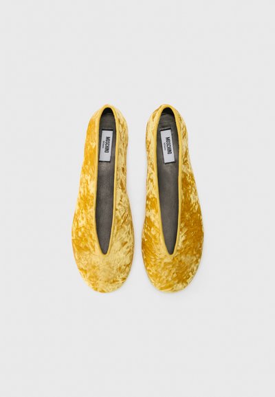 Zapatos planos amarillos de terciopelo con una textura suave, forma alargada y abertura en forma de v profunda. Forro interno gris suave. Sin hardware visible.