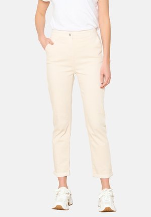 Pantaloni in cotone beige con una vestibilità slim, orli arrotolati, tasche frontali e chiusura con bottone, abbinati a sneaker bianche.