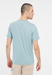 Svetlo modré tričko s krátkym rukávom vyrobené z mäkkej tkaniny, so zaobleným výstrihom a voľným strihom, zobrazené zozadu.