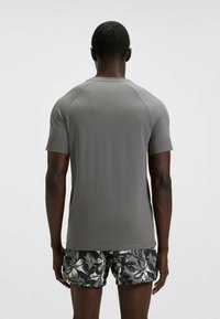 Szary, krótki rękaw sportowy shirt z okrągłym dekoltem, wykonany z gładkiej tkaniny i raglanowymi rękawami, połączony z wzorzystymi szortami kąpielowymi.