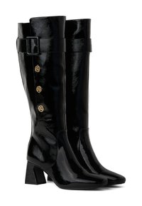 Fekete, térd fölé érő csizmák fényes felülettel, hegyes orral, tömör sarkakkal és díszes aranyszínű gombokkal a külső oldalukon.