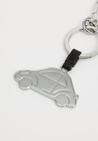 Porte-clés en métal argenté en forme de voiture, avec un accent en cuir noir. Le design comprend des contours détaillés des fenêtres et des roues.
