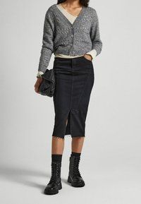 Szary, dziergany kardigan z dekoltem w serek, czarna spódnica ołówkowa z denimu z przednim rozcięciem oraz czarne, sznurowane botki typu combat. Teksturowane tkaniny i dopasowany krój.