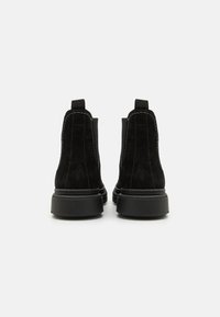 Sorte nubuck ankelstøvler med en glat finish, elastiske sidestykker og kraftige sorte gummisåler. Kontraststing langs sømmene.