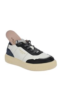 Sneaker caratterizzato da un mix di pelle bianca e suede blu navy, dettagli neri, lacci grigi e una suola spessa e rigata di colore beige. Presente un dettaglio del logo in oro.