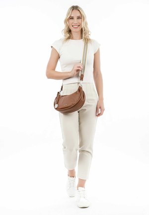 Brown leather crossbody bag with a rounded shape, textured finish, silver hardware, and adjustable strap, carried by a person in light clothing.