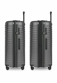 Valise gris à coque dure avec des rainures verticales, fermetures à glissière doubles, poignée latérale, poignée rétractable et quatre roues pour plus de stabilité.