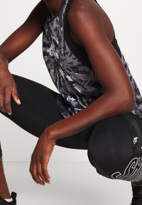 Czarny sportowy top na ramiączkach z szarym abstrakcyjnym wzorem i białym logo, zestawiony z czarnymi legginsami z dużym białym napisem.