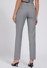 Svarta och vita rutiga byxor i slim fit, med slät textur och bakfickor, som är kombinerade med öppna klackskor.