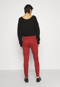 Svart stickad tröja med vid halsringning, kombinerad med röda tajta byxor med en slät textur och elastisk midja. Svarta skor fulländar outfitten.