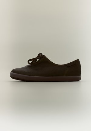 Chaussure décontractée marron foncé unique, à profil bas, embout arrondi et fermeture simple à nœud papillon sur un fond clair uni.