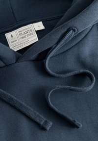 Navyblaue Kapuzenpulli aus strukturiertem Material, mit verstellbaren Kordeln und einem Etikett, das den Markennamen und Produktdetails anzeigt.