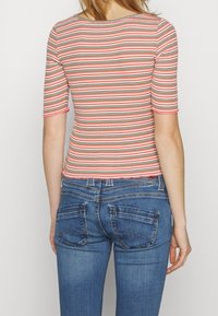 Randig topp med korta ärmar, rund halsringning och tunna röda, gröna och vita ränder, tillsammans med blå denimjeans med bakfickor.