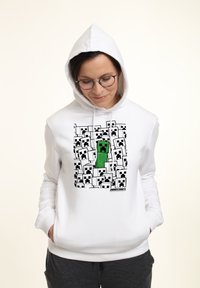 Biała bluza z kapturem z graficznym nadrukiem zielonych i czarnych postaci z gry Minecraft. Miękka tkanina o luźnym kroju i regulowanym kapturem.