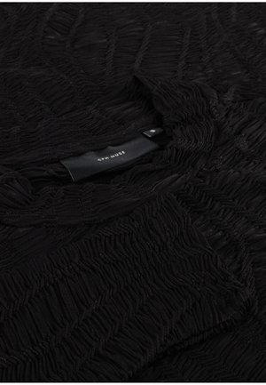 Black textured fabric with a wavy pattern, featuring a rounded neckline and a visible care label at the neckline.