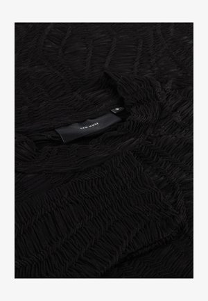 Black textured fabric with a wavy pattern, featuring a rounded neckline and a visible care label at the neckline.