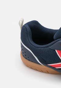 Sneaker z siateczkowej górnej części w kolorze granatowym, białymi akcentami i czerwonymi detalami. Gumowa podeszwa z otworami wentylacyjnymi oraz uchwytem na pięcie.