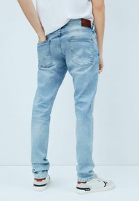 Vaaleansiniset farkut, joissa on kapea malli, viisi taskua ja takana ruskea nahkapaikka. Yhdistetty valkoisiin lenkkareihin.