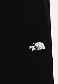 Mustat kangasta olevat jogginghousut, joissa on valkoinen "The North Face" -logo ja näkyvät saumat, tarjoavat tyylikkään muotoilun.
