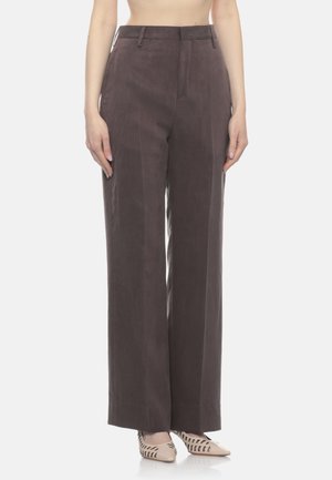 Donna che indossa pantaloni marrone scuro a vita alta e gamba larga abbinati a décolleté beige con punta appuntita e dettagli traforati.