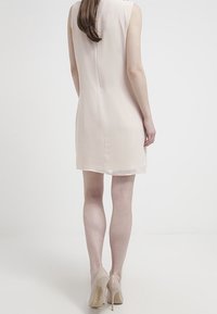 Robe sans manches couleur blush à coupe droite, texture douce et longueur au genou. Associée à des escarpins nude et peu de détails.