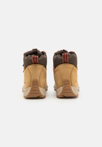 Brown leather boots with tan accents, high-top design, padded collar, and rubber sole. Features red logo tag at the back for added detail.