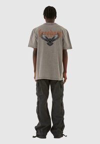 Grå oversized t-shirt med et sort ørn grafik og teksten "frihed" på ryggen, parret med sorte cargo bukser med lommer.