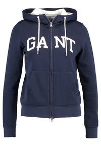 Felpa con zip blu navy realizzata in misto cotone. Presenta un logo bianco "GANT" sul petto, tasche frontali e coulisse sulla cappuccio.
