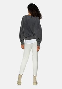 Sudadera de gran tamaño en gris oscuro con hombros caídos, dobladillo acanalado y cuello redondo, combinada con pantalones blancos ajustados y botas beige hasta el tobillo.