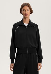 Fekete zipzáras dzseki látványos gallérral, bordás mandzsettákkal és szegéllyel. Fehér díszvarrás található a vállak mentén. Finom, puha anyagból készült.