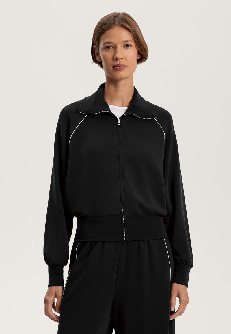 Čierna mikina na zips s golierom, rebrovanými manžetami a spodným lemom. Má biele kontrastné lemovanie na pleciach. Vyrobená z hladkej, jemnej látky.