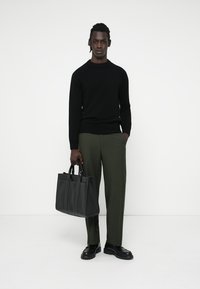 Czarny dzianinowy sweter, oliwkowe spodnie, czarna skórzana torba na ramię i czarne buty. Prosty design z subtelnymi fakturami i czystymi liniami.