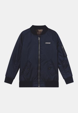 Námořnická modrá bomber bunda se zipem, žebrovaným límcem a manžetami, dvěma předními kapsami a kapsou se zipem na rukávě. Hladká, lesklá textilie.