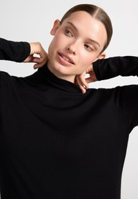 Sort turtleneck-top lavet af et blødt, strækbart stof. Har lange ærmer med tætsiddende manchetter og en afslappet pasform omkring halsudskæringen.