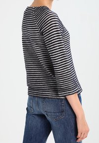 Haut en maille rayé bleu marine et blanc, avec un col arrondi et des manches trois-quarts. Associé à un jean denim bleu.