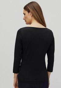 Svart långärmad skjorta med en lätt båthalsning och en mjuk textur, med en enkel design och en åtsittande silhuett.