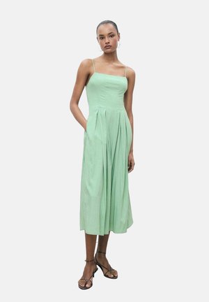 Abito midi verde con spalline sottili, corpino aderente, gonna plissettata e tasche. Realizzato in tessuto leggero con una trama morbida.