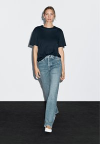 T-shirt noir à manches courtes associé à un jean droit taille haute bleu clair, complétant le look avec des chaussures plates blanches.