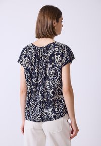 Blusa corta a maniche corte floreale navy con scollo arricciato e dettagli bianchi. Presenta una vestibilità comoda e un tessuto leggero.